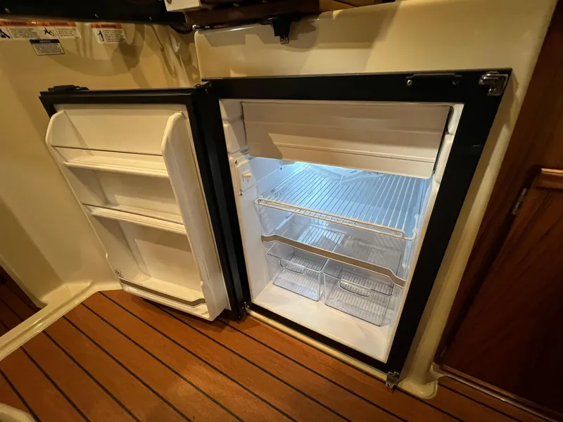 Slide: The Image of 2023 Ranger Tugs R-25 interior fridge with open door, showcasing shelves and storage space. - 11