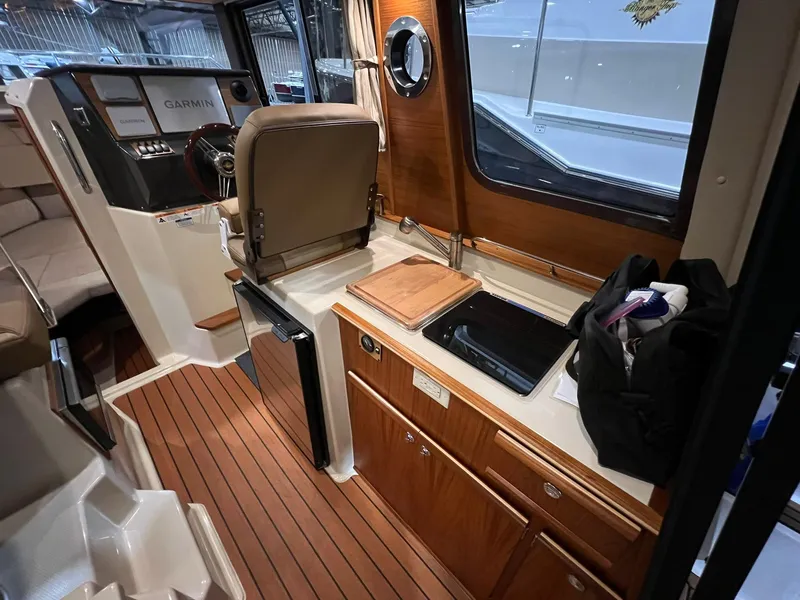 Slide: The Image of 2023 Ranger Tugs R-25 interior with helm, kitchenette, and wood accents. - 16