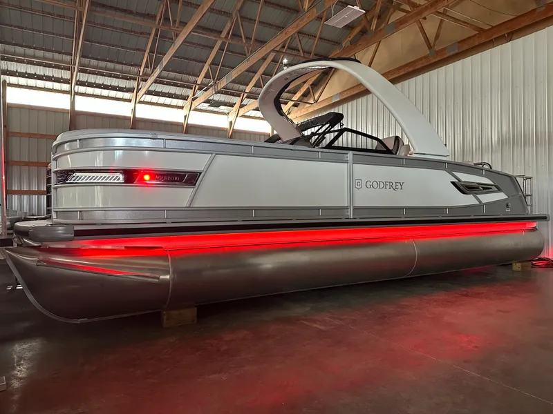 Slide: The Image of 2025 Godfrey AquaPatio 255 SFLW pontoon boat with red LED lights in a warehouse. - 2