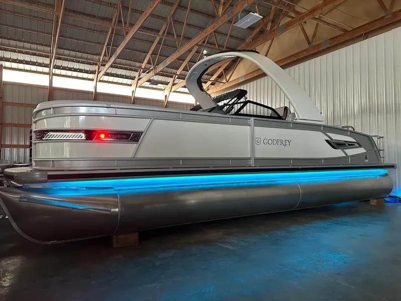 Slide: The Image of 2025 Godfrey AquaPatio 255 SFLW pontoon boat with blue underglow lighting in a warehouse. - 37