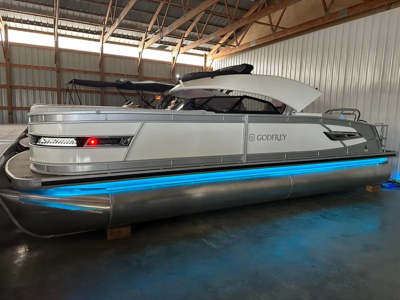 Slide: The Image of 2025 Godfrey AquaPatio 255 SFLW pontoon boat with blue LED lights in a warehouse. - 7