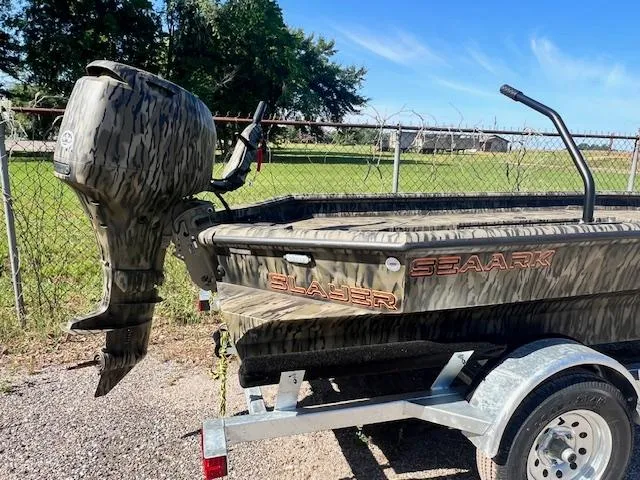 Slide: The Image of 2025 SeaArk 1752 Slayer Pro boat on trailer, camo design, parked outdoors. - 2