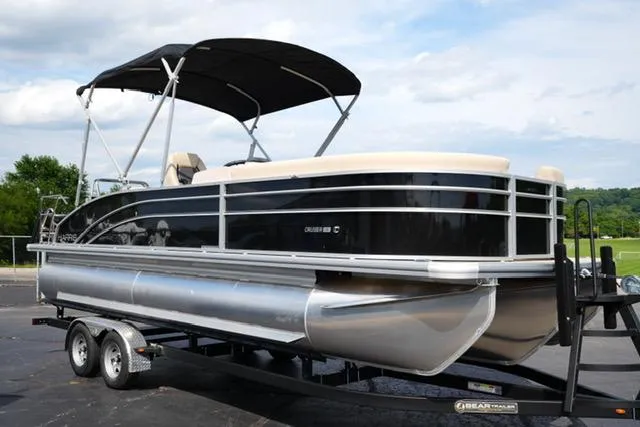 Slide: The Image of 2025 Harris Cruiser 230 pontoon boat on trailer, black and silver design, parked outdoors. - 2