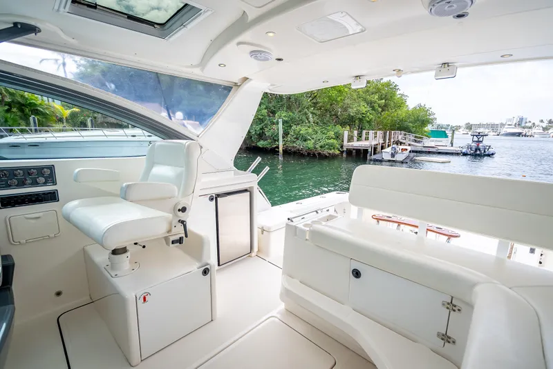 Slide: The Image of 2005 Tiara Yachts 4200 Open interior, featuring helm and seating, docked by a scenic waterfront. - 33