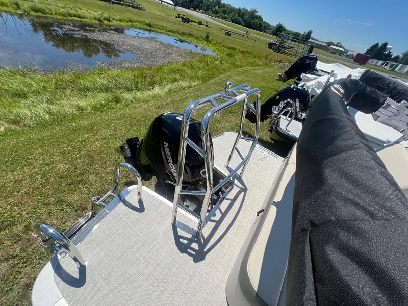 Slide: The Image of 2024 Harris FloteBote Sunliner 230 pontoon boat with motor and railing, parked on grass. - 17