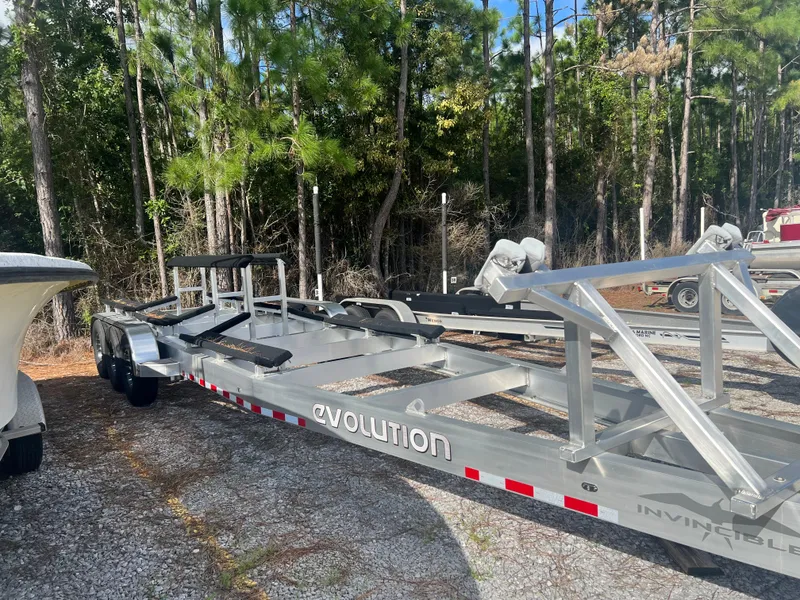 Slide: The Image of Trailer for 2024 Invincible 33 Catamaran, parked outdoors on gravel, surrounded by trees. - 44