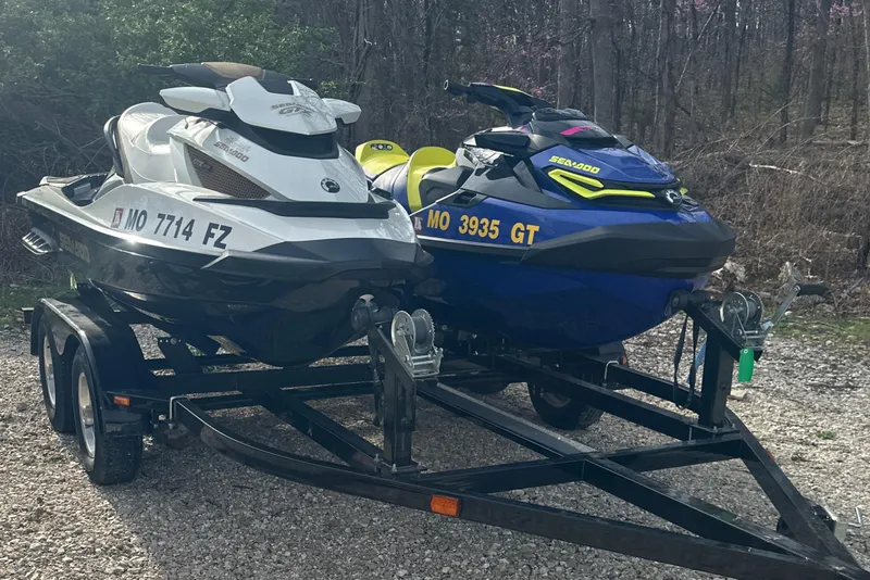 Slide: The Image of Two Sea-Doo jet skis, including a 2021 Wake Pro 230, on a trailer in a wooded area. - 2