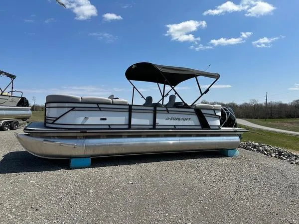 The Image of 2023 Starcraft SLS-3 pontoon boat with canopy on gravel, under a clear blue sky. - 1
