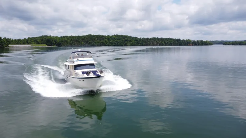 Slide: The Image of 1987 Hatteras 63 Motor Yacht cruising on a serene lake under cloudy skies. - 2