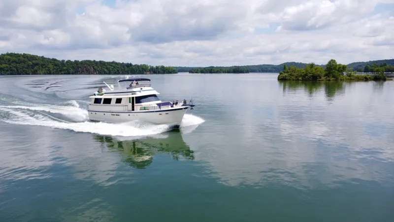 Slide: The Image of 1987 Hatteras 63 Motor Yacht cruising on a serene lake under cloudy skies. - 4