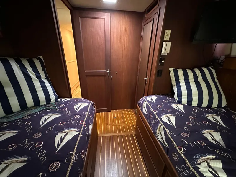 Slide: The Image of 1987 Hatteras 63 Motor Yacht cabin with twin beds, nautical bedding, and wood paneling. - 49