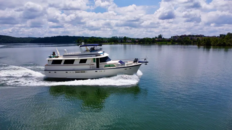 Slide: The Image of 1987 Hatteras 63 Motor Yacht cruising on a serene lake under a partly cloudy sky. - 6