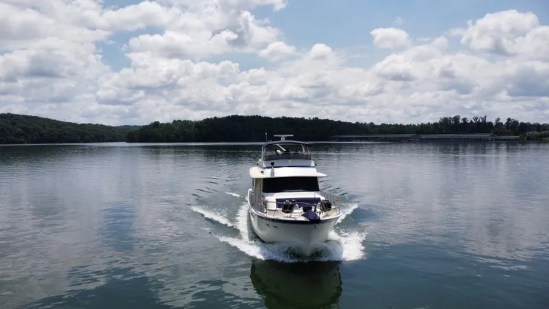 Slide: The Image of 1987 Hatteras 63 Motor Yacht cruising on a serene lake under a cloudy sky. - 8
