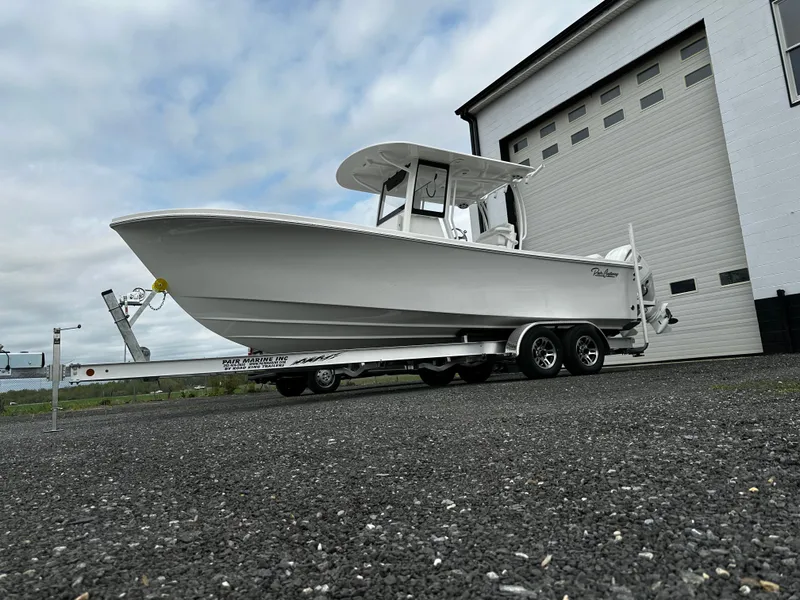 Slide: The Image of 2025 Pair Customs 24OS boat on trailer, parked outside a garage. - 0