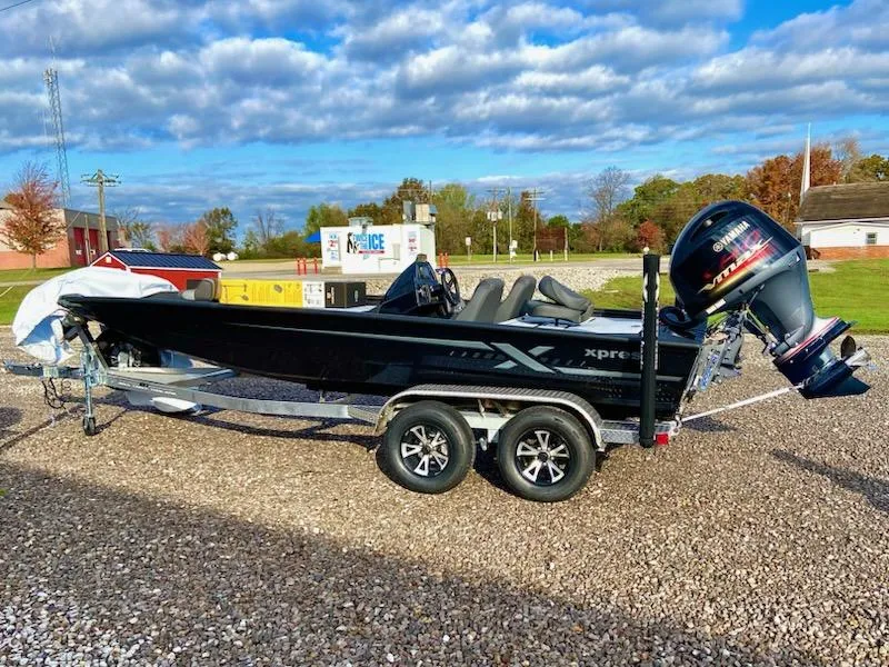The Image of 2025 Xpress H20 Bass boat on trailer, parked outdoors under a partly cloudy sky. - 1