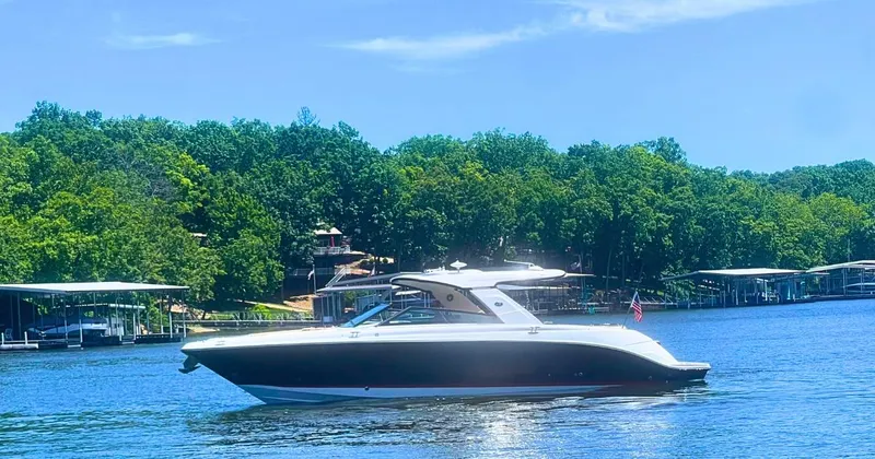 Slide: The Image of 2022 Sea Ray 400 SLX boat cruising on a sunny lake with lush green trees. - 0