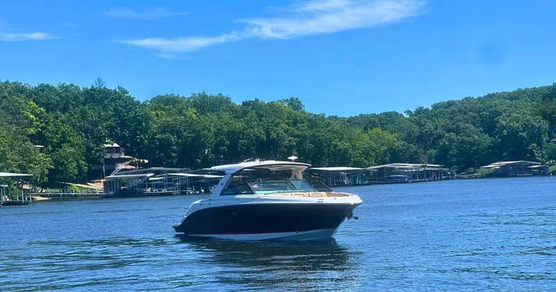 Slide: The Image of 2022 Sea Ray 400 SLX boat cruising on a serene lake with lush green shoreline. - 2