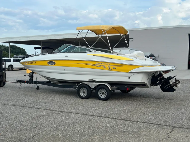 Slide: The Image of 2006 Crownline 240 EX boat with yellow accents on a trailer, parked outdoors. - 0