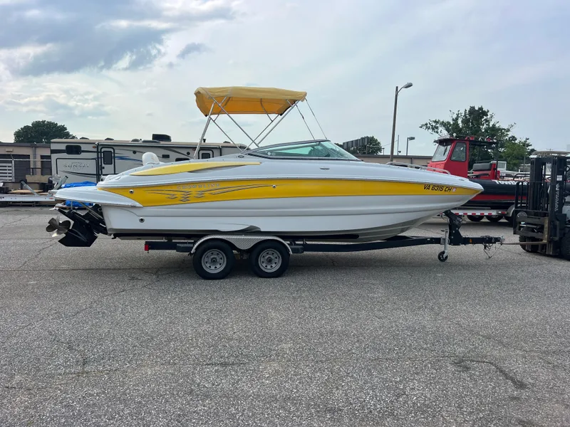 Slide: The Image of 2006 Crownline 240 EX boat with yellow accents on a trailer, parked outdoors. - 1
