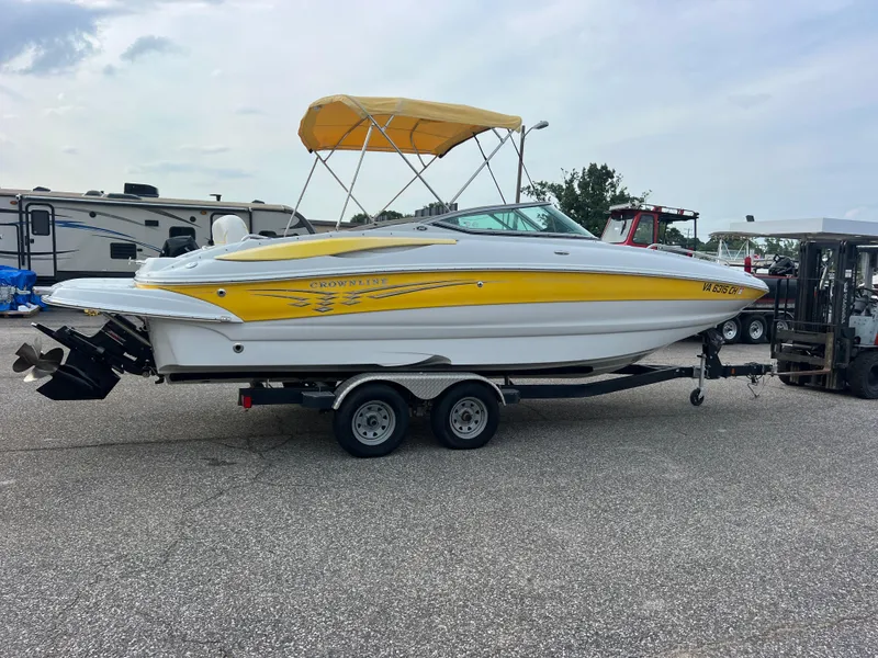 Slide: The Image of 2006 Crownline 240 EX boat with yellow accents on a trailer, parked outdoors. - 2