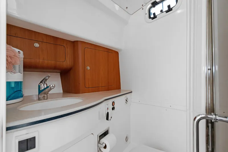 Slide: The Image of 2004 Intrepid 377 Walkaround boat bathroom with sink, wooden cabinets, and porthole window. - 36