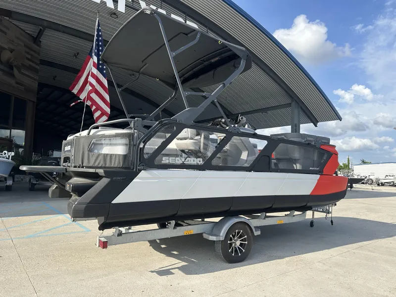 Slide: The Image of 2023 Sea-Doo Switch Cruise 21' boat on trailer, parked outdoors with American flag. - 7