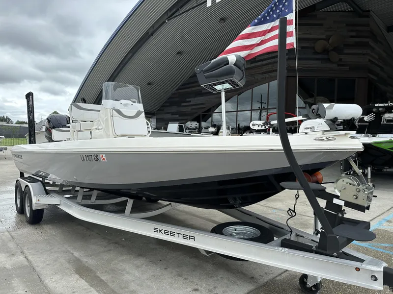 Slide: The Image of 2023 Skeeter SX230 boat on trailer with American flag, parked outside a modern building. - 15