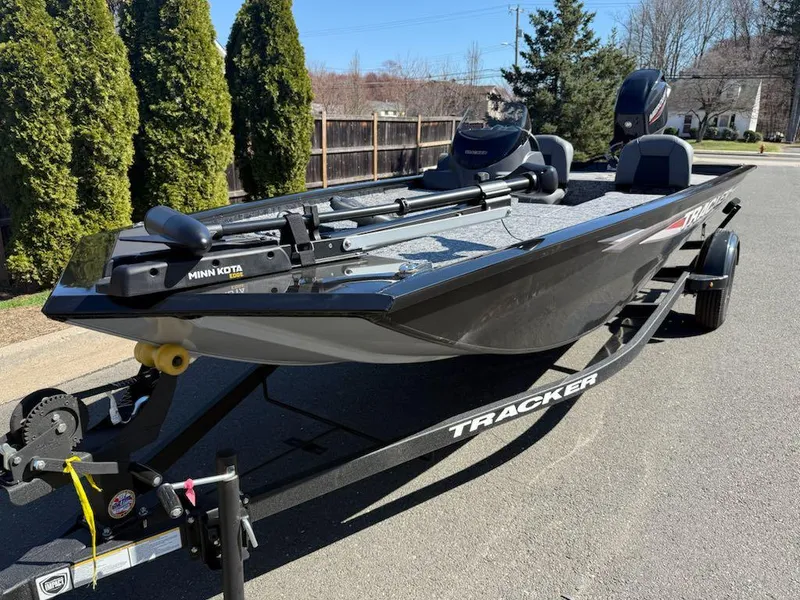 Slide: The Image of 2025 Tracker Pro Team 175 boat on trailer, parked outdoors, featuring Minn Kota trolling motor. - 2