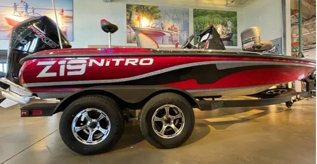The Image of 2025 Nitro Z19 boat in showroom, red and black design, dual axle trailer. - 0