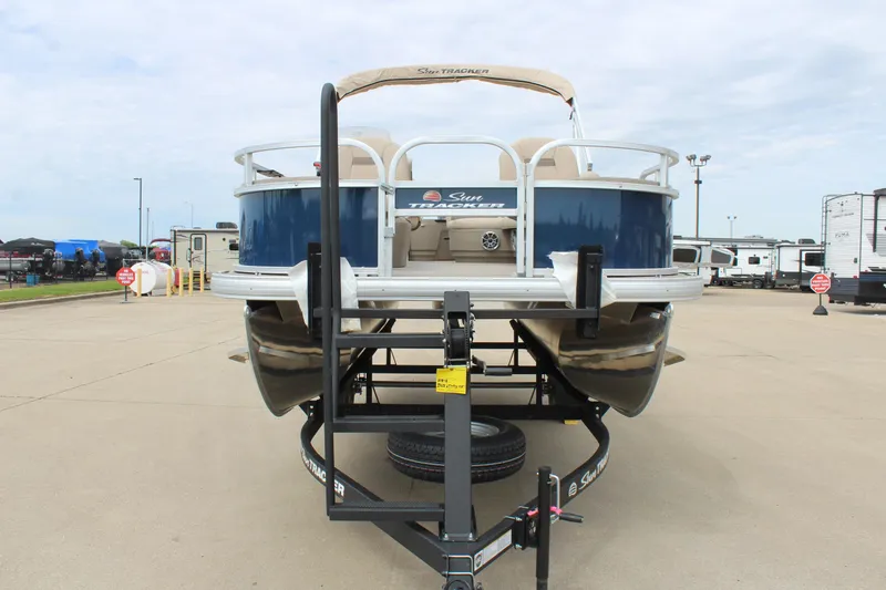 Slide: The Image of 2025 Sun Tracker Bass Buggy 18 DLX pontoon boat on trailer, parked outdoors. - 2