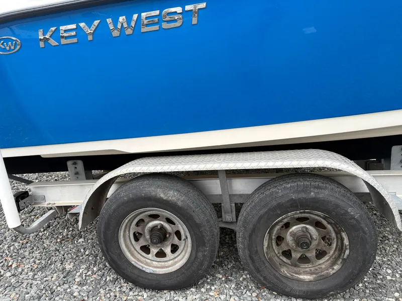 Slide: The Image of Blue 2017 Key West 219fs boat on a dual-axle trailer with gravel background. - 6