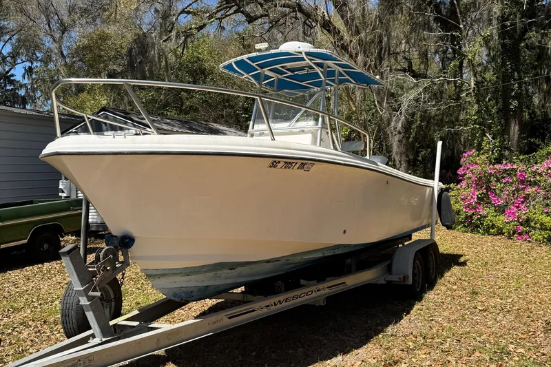 Slide: The Image of 2002 Edgewater 225CC boat on trailer, parked outdoors with trees and flowers in the background. - 0