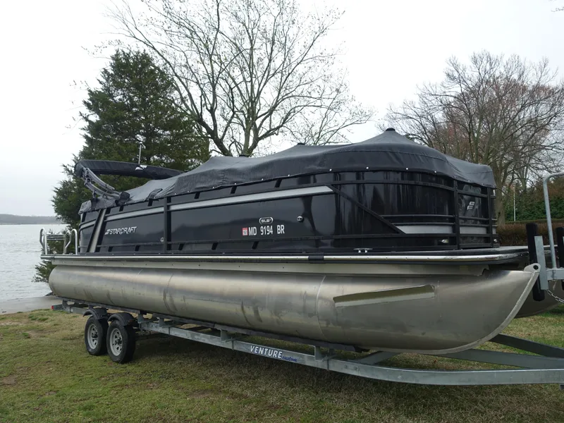 Slide: The Image of 2021 Starcraft SLS 5 DC pontoon boat on trailer, covered, near a lake. - 1