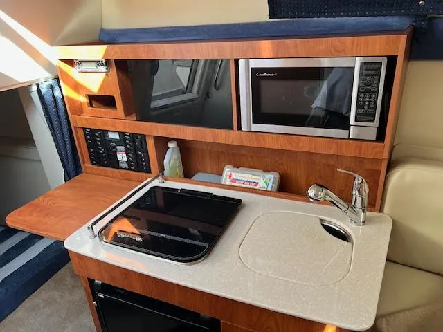 Slide: The Image of 2009 Bayliner 245 Cruiser interior with kitchenette, featuring sink, stove, and microwave. - 11