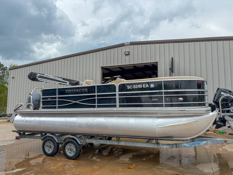 Slide: The Image of 2018 Trifecta 22 C CS 2.75 pontoon boat on trailer, parked outside a warehouse. - 7