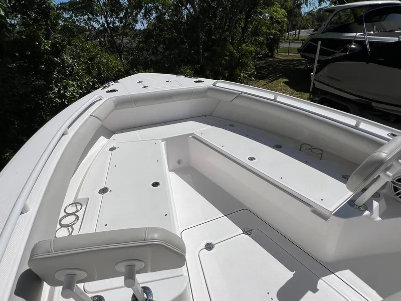 Slide: The Image of 2022 Everglades 273 CC boat interior with seating and storage, surrounded by trees. - 17