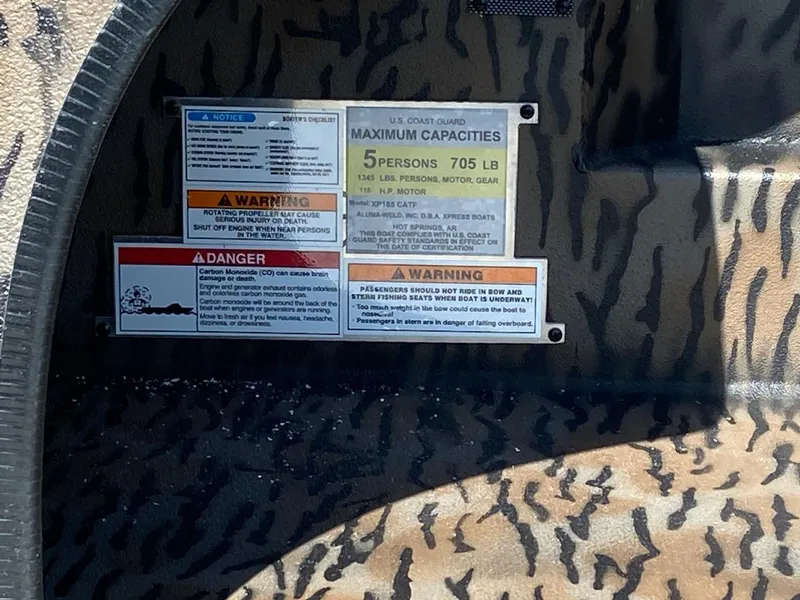 Slide: The Image of 2024 Xpress XP185 Catfish boat capacity and safety warning labels on camouflage interior. - 11