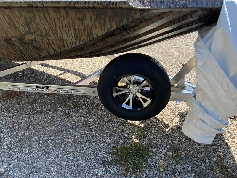 Slide: The Image of 2024 Xpress XP185 Catfish boat trailer with camouflage design and shiny wheel on gravel. - 15