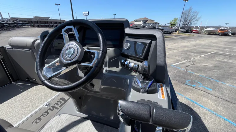 Slide: The Image of 2024 Tahoe Pontoon 2585 Cascade dashboard with steering wheel and controls in a parking lot. - 34