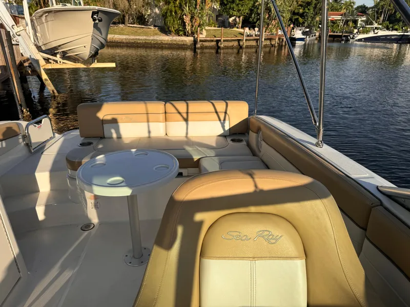 Slide: The Image of 2011 Sea Ray 280 Sundeck interior with tan seating and table, docked by a calm waterfront. - 5