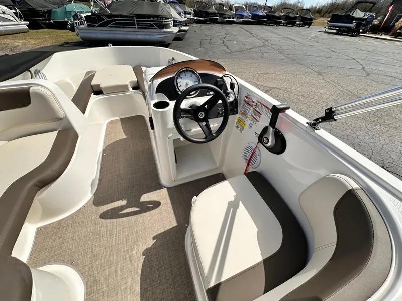 Slide: The Image of 2023 Bayliner Element 18 Deck Boat interior with steering wheel and seating, parked outdoors. - 2