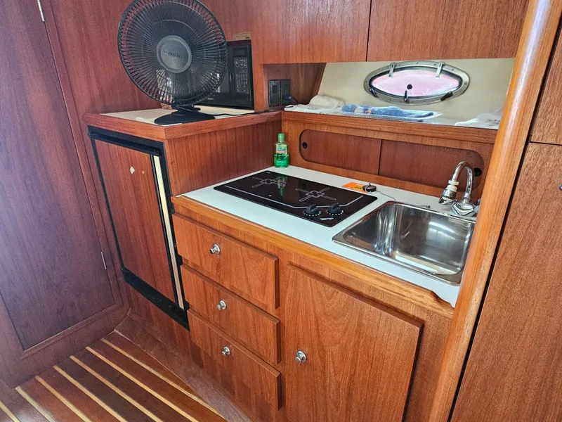 Slide: The Image of 2000 Tiara Yachts 3100 Open kitchen with wooden cabinetry, sink, stove, and fan. - 21