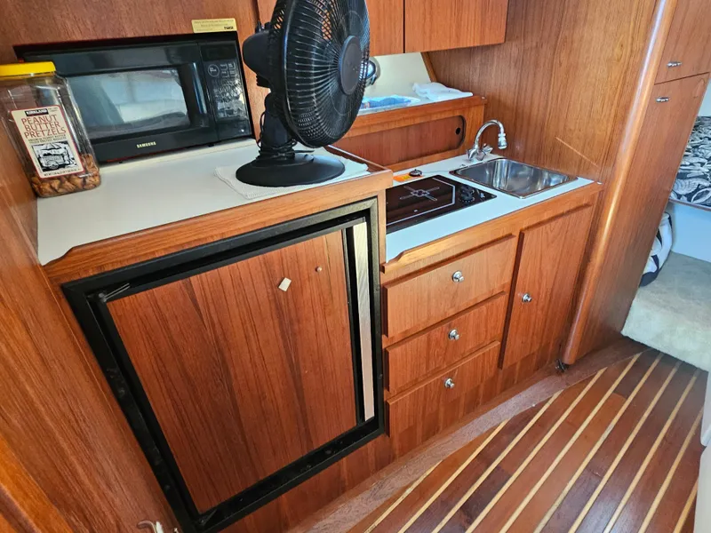 Slide: The Image of 2000 Tiara Yachts 3100 Open galley with wood cabinetry, sink, microwave, and fan. - 22