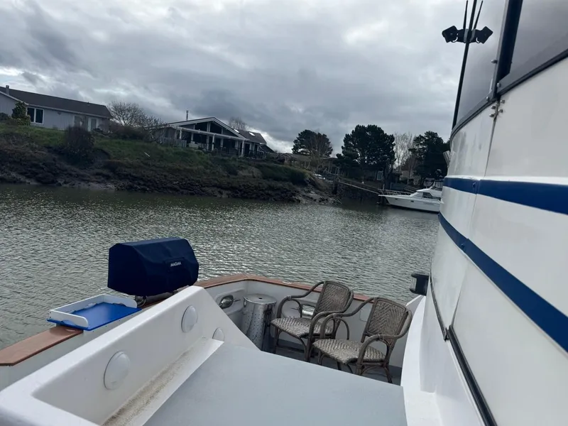 Slide: The Image of 1989 Prima 52 Cockpit Motor Yacht docked by a serene riverside with outdoor seating. - 10