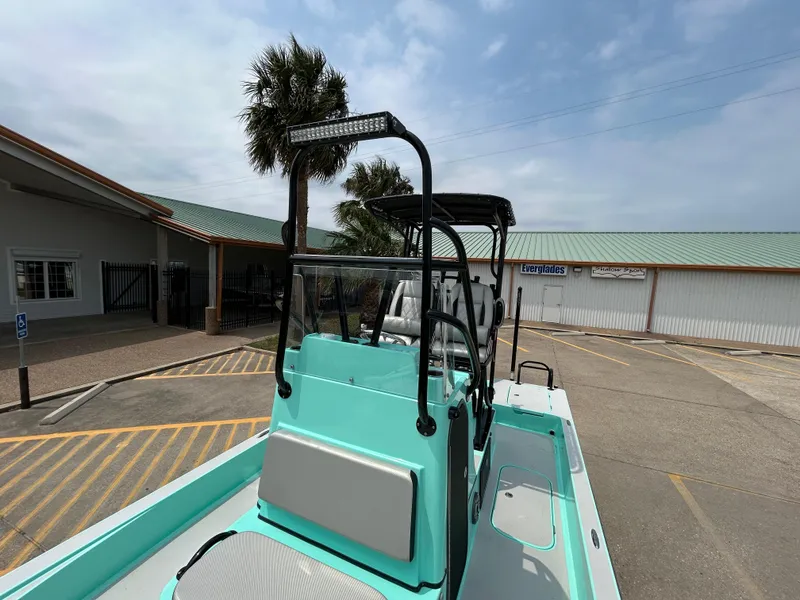 Slide: The Image of 2022 Shallow Sport 25 X3 boat with teal accents, parked near a building. - 13