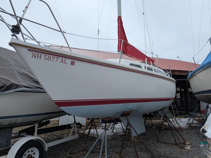 The Image of 1983 Catalina 27 sailboat on stands, red trim, white hull, in a boatyard. - 0