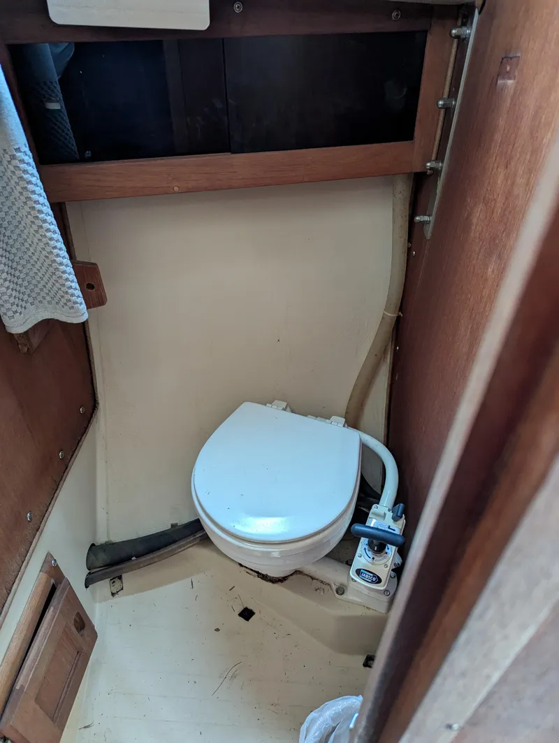 Slide: The Image of 1983 Catalina 27 boat bathroom with compact marine toilet and wooden cabinetry. - 12