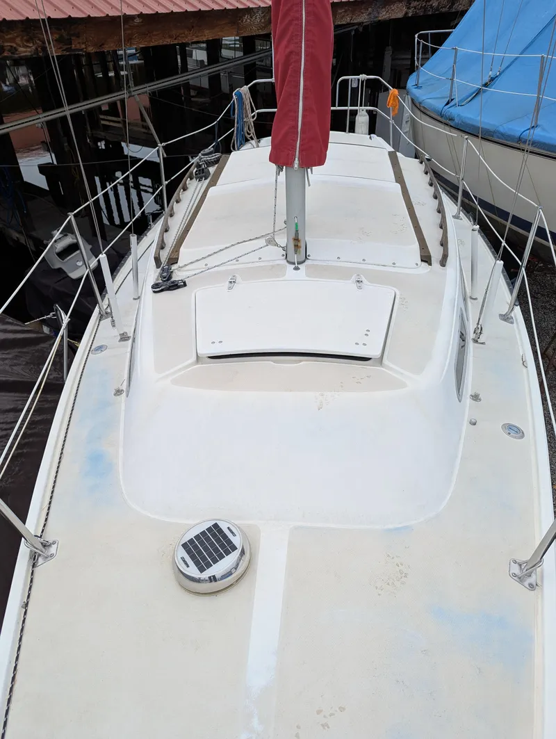 Slide: The Image of 1983 Catalina 27 sailboat deck with red sail cover, docked near other boats. - 2