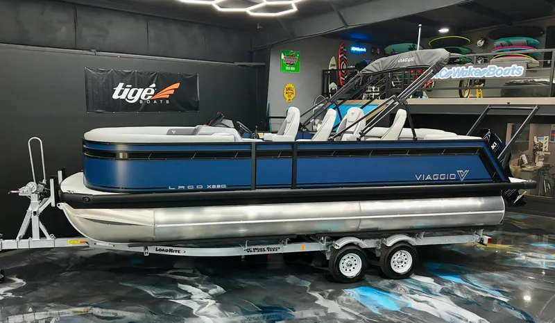 Slide: The Image of 2025 Viaggio Lago X-Q pontoon boat on trailer in showroom setting. - 0