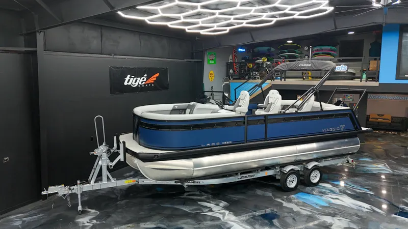 Slide: The Image of 2025 Viaggio Lago X-Q pontoon boat on trailer in showroom with modern lighting. - 6